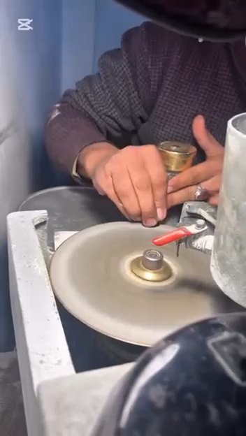 Hands guiding a stone against a spinning polishing wheel at the workshop