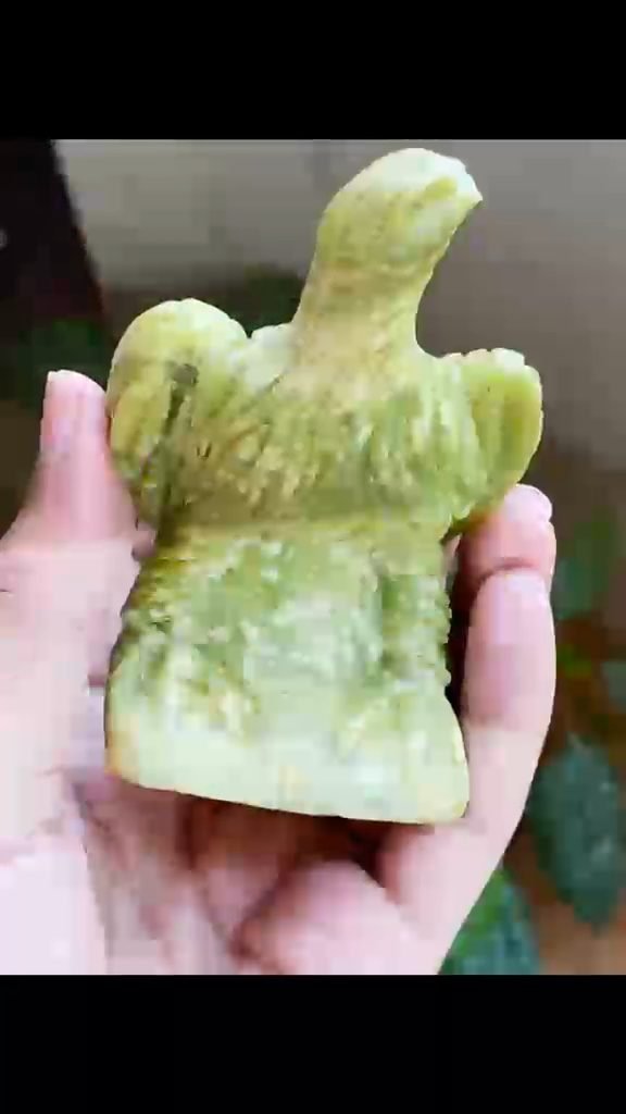Hand holding a small eagle figure carved from natural green stone