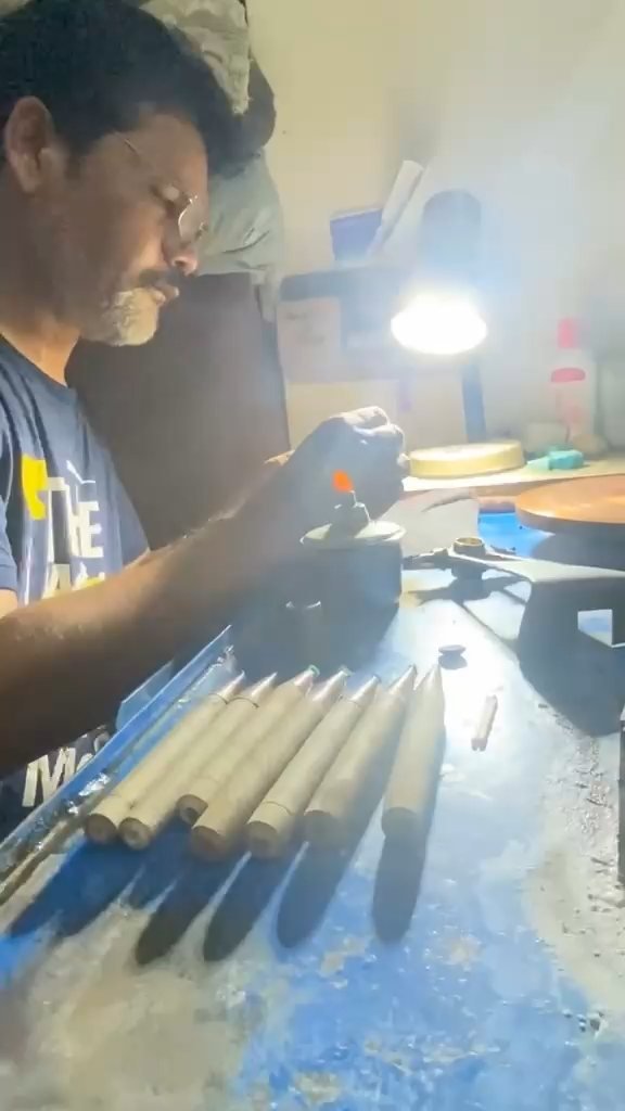 Craftsman warming a cutting stick over a small flame at the workshop bench, with mounted gemstones laid out in a row